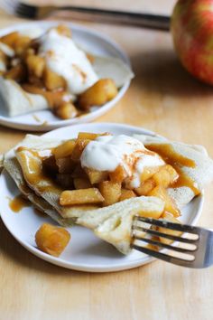 two white plates topped with food on top of a wooden table next to a fork