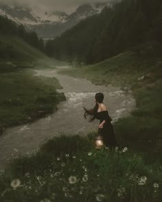 a woman in black dress standing next to a river