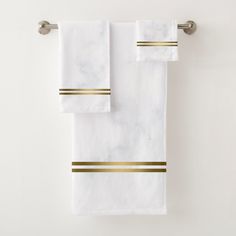 two white towels with gold stripes hanging on a towel rack in front of a wall