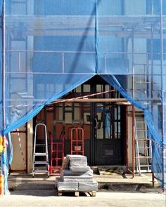 a building under construction with blue tarp covering the front door and side entrance area