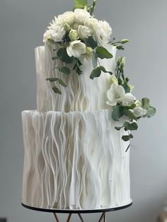 a three tiered white wedding cake with flowers on top and greenery in the middle