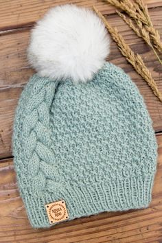 a knitted hat with a white pom - pom sits on a wooden surface