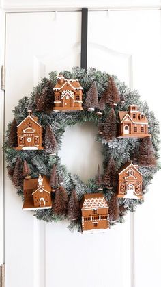 a wreath is hanging on the front door with small houses and fir trees around it