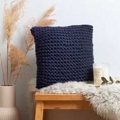 a blue crocheted pillow sitting on top of a wooden bench next to a vase