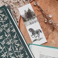 an open book on a wooden table next to a card with a drawing of a horse