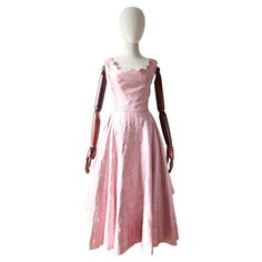 This truly spectacular 1950's dress, rendered in a blush pink satin which is embroidered with pink lurex and cream threads in a swirling floral design, set against layers of matching pink tulle, which is framed by scalloped edging, is the perfect piece for your vintage collection. The wide square neckline is framed by scalloped petal edges, along the front and back of the dress, which set off the sleeveless cut. The fitted bodice, is accented by tailored darts, which run from below the bust-line and set off the cinched in waistline, which boasts a pipped detail in matching fabric. The full circle cut of the skirt, is accepted by elegant draped pleats along each side, which set off the scalloped edges of the satin top layer of the shirt, which draws in along the back of the waistline with a Tiered Tulle Dress, 1950's Dress, Tiered Tulle Skirt, Elegant Drapes, Rose Blush, Pink Tulle, Vestidos Vintage, 1950s Dress, Satin Top