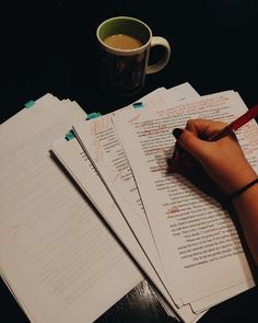 a person writing on paper with a cup of coffee in the background