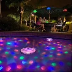 people sitting at a table in the middle of a pool with colorful lights on it