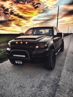 the truck is parked on the side of the road with its lights on at sunset