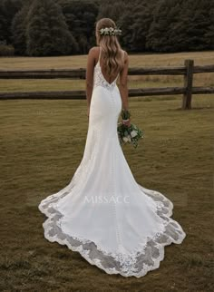 a woman in a white wedding dress standing on the grass with her back to the camera