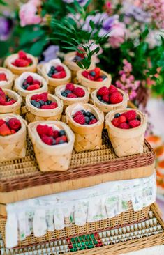 an arrangement of fruit in baskets on top of a wicker cake stand with flowers and greenery behind it