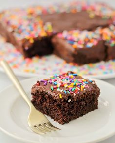 a slice of chocolate cake with sprinkles on a white plate next to a fork