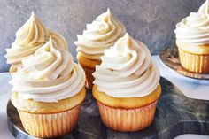 three cupcakes with white frosting sitting on top of a marble platter