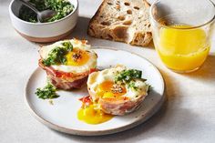 two eggs are sitting on a plate next to some bread and orange juice in a bowl