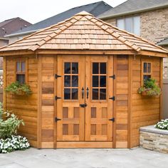 a wooden shed with two doors and window boxes on the side of it in front of a house