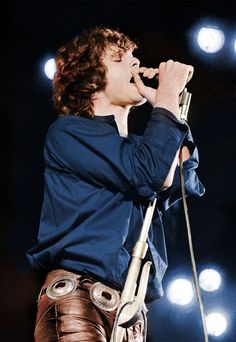 a young man singing into a microphone while standing in front of some lights on stage