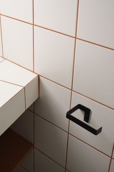 the corner of a bathroom with white tiles and brown trim on the wall, has a black square handle