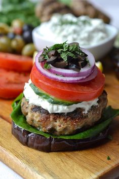 a close up of a hamburger on a cutting board with tomatoes, onions and lettuce