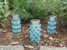 three blue glass vases sitting on the ground in front of some bushes and plants