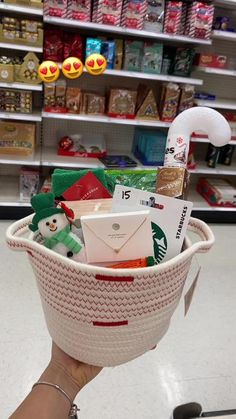 someone is holding up a basket full of christmas items in a store with other gifts on the shelves behind them