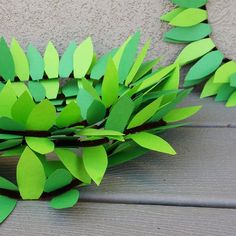 some green leaves are laying on a wooden table and one is cut out from paper