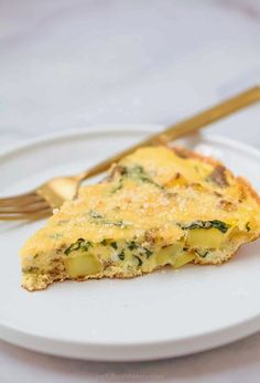 a slice of quiche on a white plate with a gold fork next to it