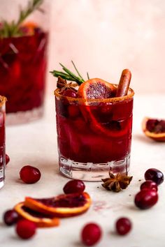 two glasses filled with cranberry punch and garnished with cinnamon, orange slices and rosemary