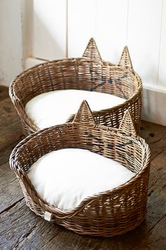 two wicker baskets sitting on top of a wooden floor next to each other with white pillows