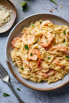 pasta with shrimp and parsley in a bowl next to silverware on a table