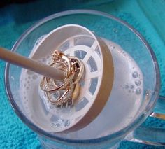 there is a ring holder in the middle of a glass container with water and gold rings on it