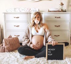 a pregnant woman sitting on the floor in front of a sign reading ready to pop