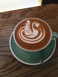 a cappuccino in a green cup sitting on top of a wooden table