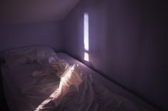 an unmade bed in a small room with sunlight coming through the window and shadows on the wall