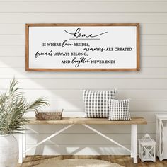 a wooden sign hanging on the side of a wall next to a white bench and potted plant