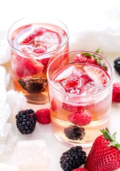 two glasses filled with ice and raspberries on top of a white tablecloth