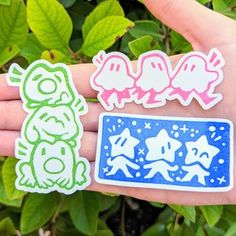 three stickers on someone's hand with green leaves in the background and blue sky