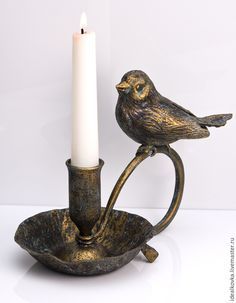 a candle holder with a bird sitting on top of it next to a lit candle