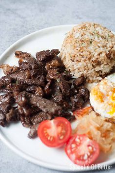 a white plate topped with meat, rice and tomatoes next to an egg on top of it