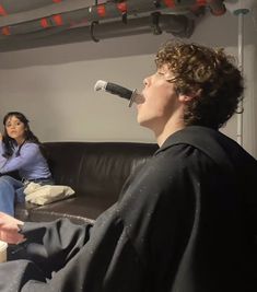 two people are sitting on a couch with microphones in their mouths and one person is drinking from a cup