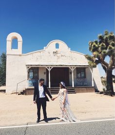 a man and woman holding hands in front of a building with palm trees on the side