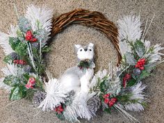 a white teddy bear sitting on top of a wreath with pine cones and red berries