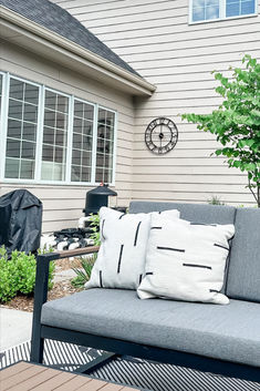 a couch sitting on top of a wooden deck next to a tree and bushes in front of a house