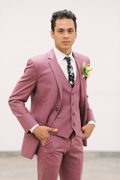 a young man in a pink suit and flower boutonniere stands with his hands on his hips