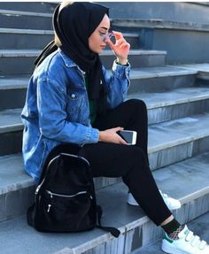 a woman sitting on the steps with her cell phone in her hand and wearing a blue jean jacket