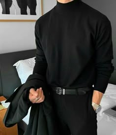 a man standing in front of a bed wearing a black turtle neck sweater