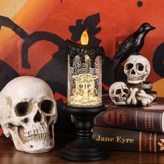 three skulls and two candles are on a table with some books in front of them