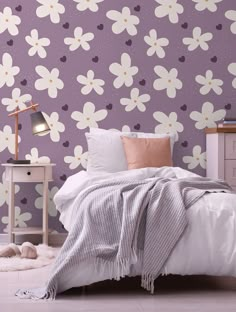 a white bed sitting next to a purple wall with flowers painted on it's walls