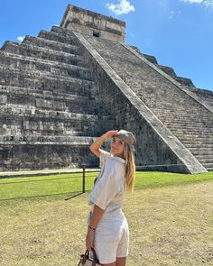 a woman is standing in front of an ancient pyramid with her hand on her head