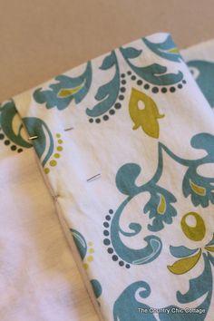 two teal and yellow patterned napkins sitting on top of a white table cloth