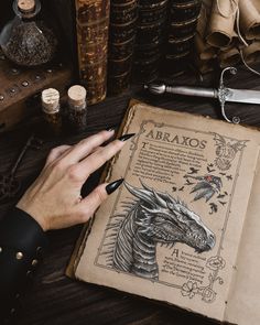 a person is writing on an old book with a dragon drawn on the front cover